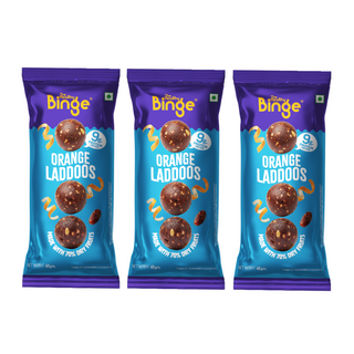 Three packages of The Binge Orange Laddoos arranged side by side on a plain white background. Each package is purple and blue with images of three orange-flavored laddoos.